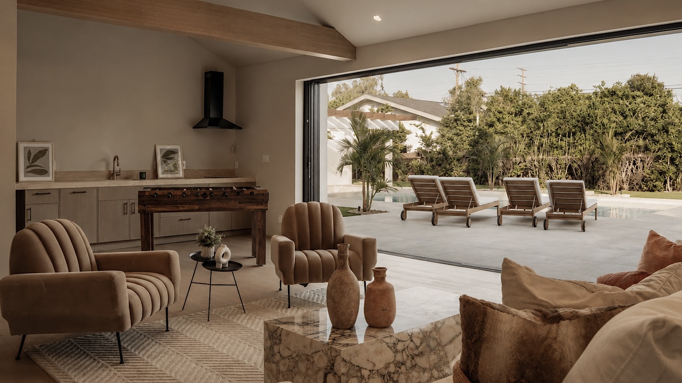 Indoor lounge with marble coffee table, channel-tufted armchairs and folding glass wall opening to a pool terrace