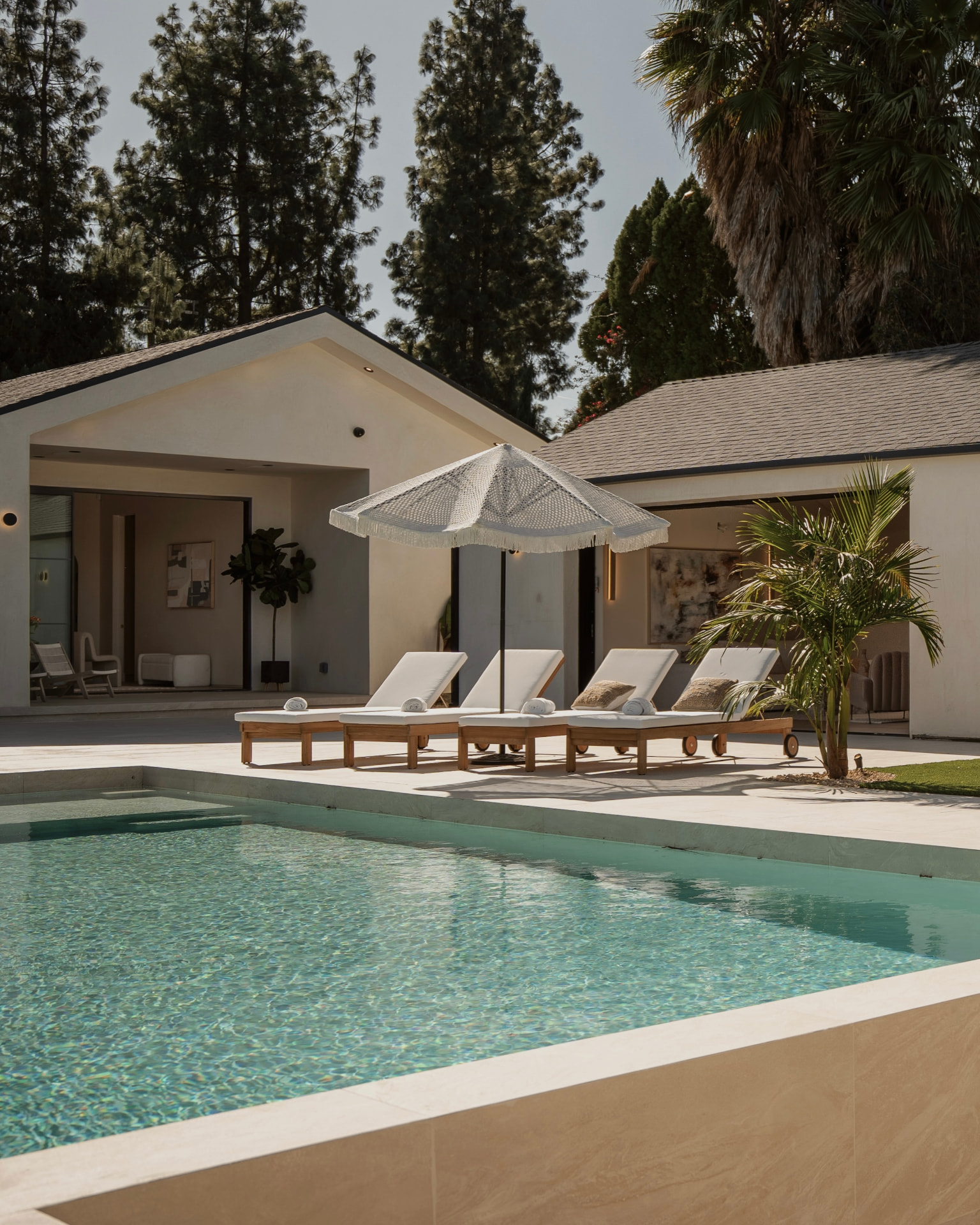Sunlit poolside terrace with teak loungers, fringed umbrella and modern California residence